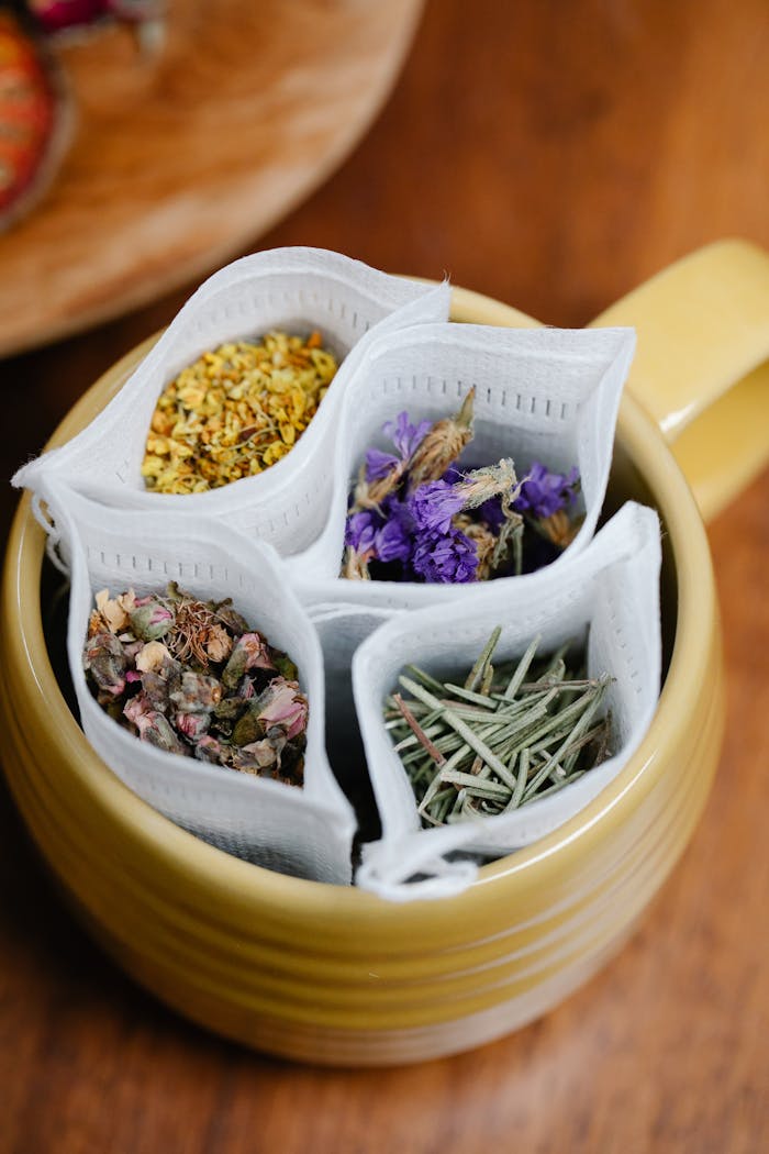 Top view of various herbal teabags with flowers in a yellow mug on a wooden table.